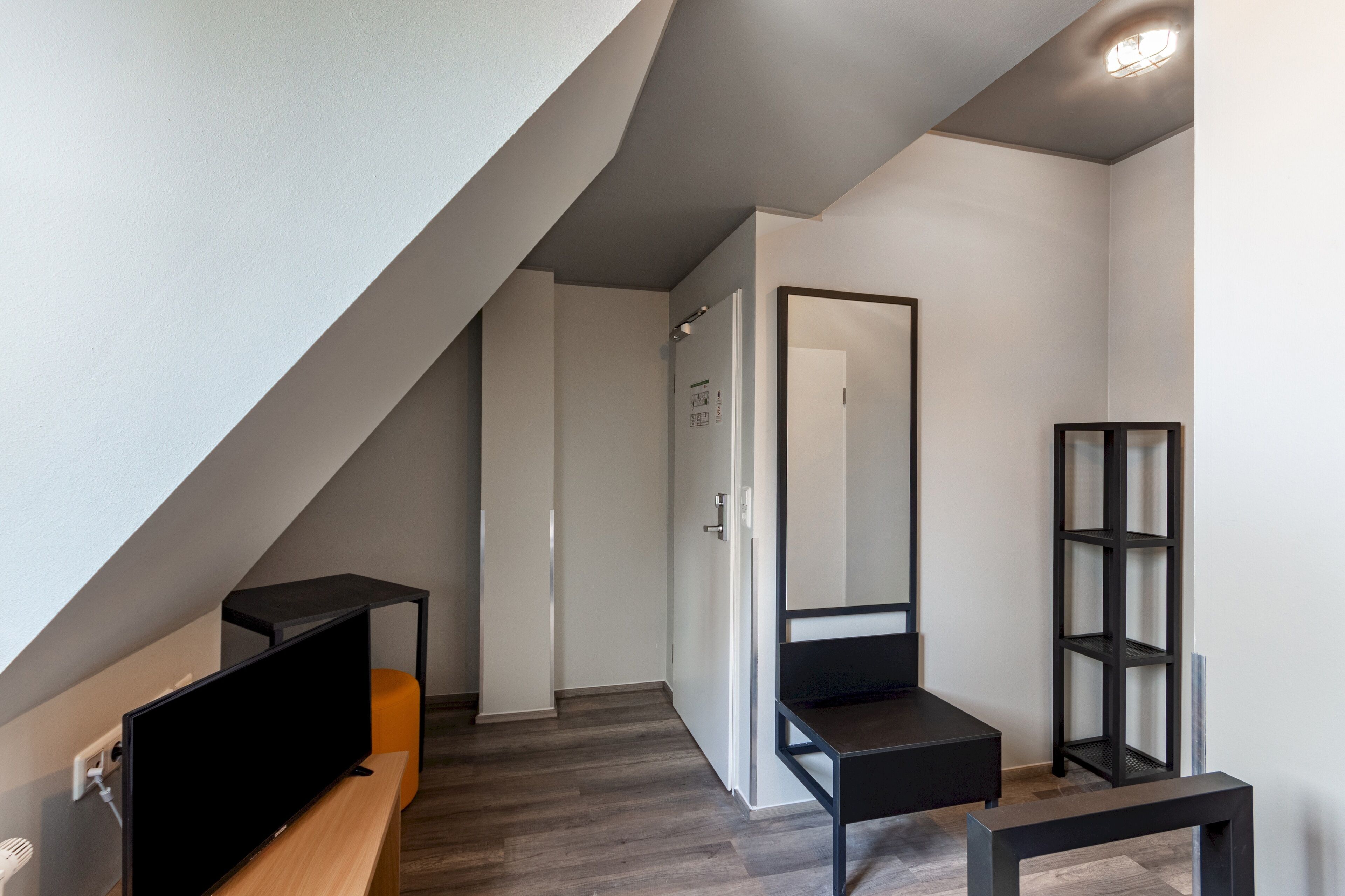 A modern, minimalistic room with a wooden bench, a black TV stand, and a black shelving unit.
