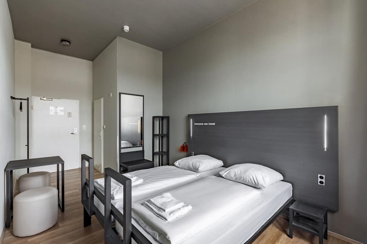 A modern hotel room with a large bed, bedside tables, a mirror, and a small stool.
