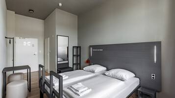 Una habitación de hotel moderna con una cama grande, mesitas de noche, un espejo y un taburete pequeño.