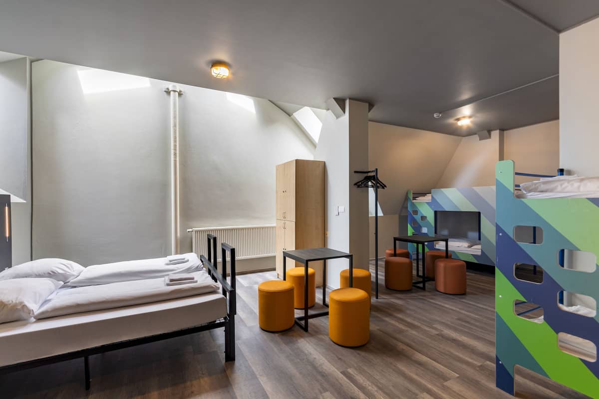 A modern, well-lit room with a bunk bed, a desk, and a chair. There are three yellow ottomans and a radiator.