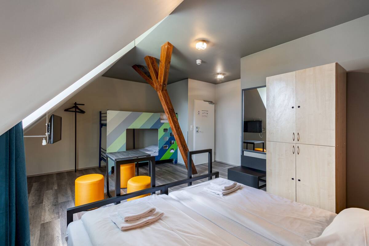 A modern hotel room with a bunk bed, a desk, a wardrobe, and a unique wooden structure.