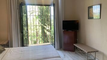 Una habitación con cama, televisor en un mueble y vista a plantas a través de una ventana.