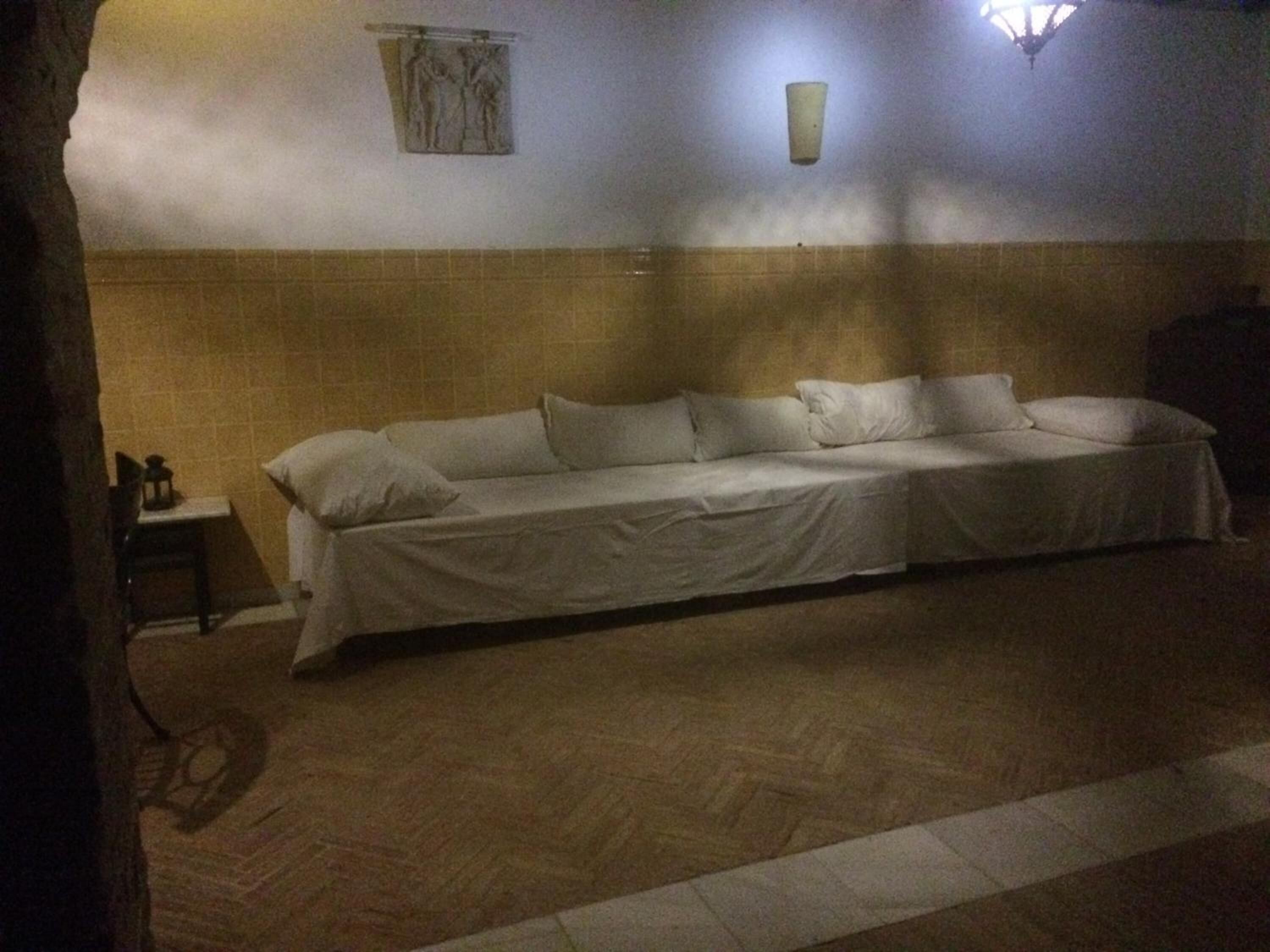 Una habitación tenuemente iluminada con una cama individual, una mesita pequeña y una lámpara fijada a la pared.