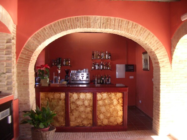 Una zona de bar con un arco de piedra, una máquina de café y estantes llenos de botellas de licores.
