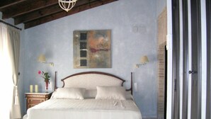 A bedroom with a large bed, two bedside lamps, a nightstand with a vase, and a painting on the wall. - Hacienda Los Jinetes (Carmona)