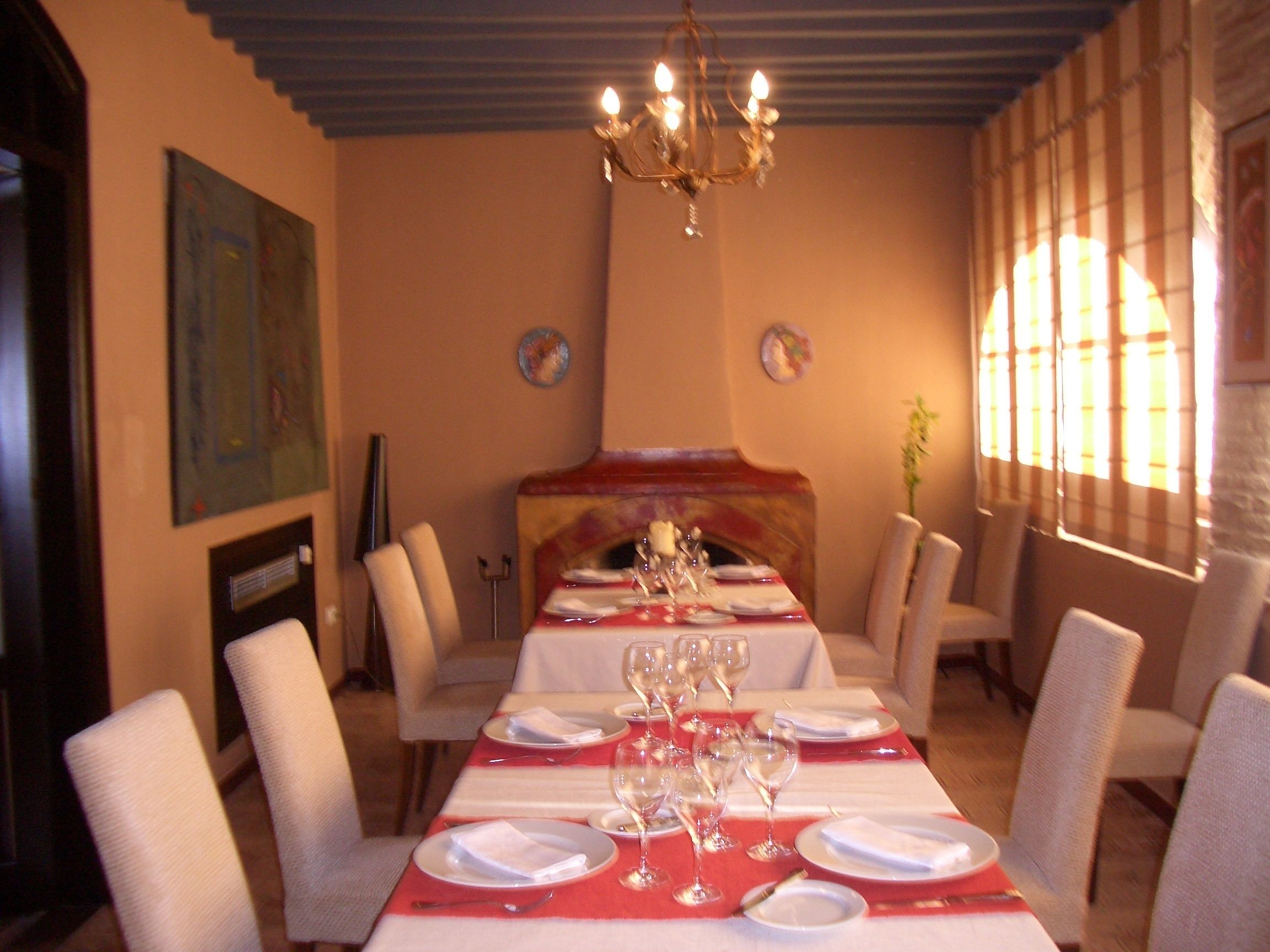 Un espace repas avec une longue table dressée pour le repas, des chaises disposées autour, et un lustre au-dessus.