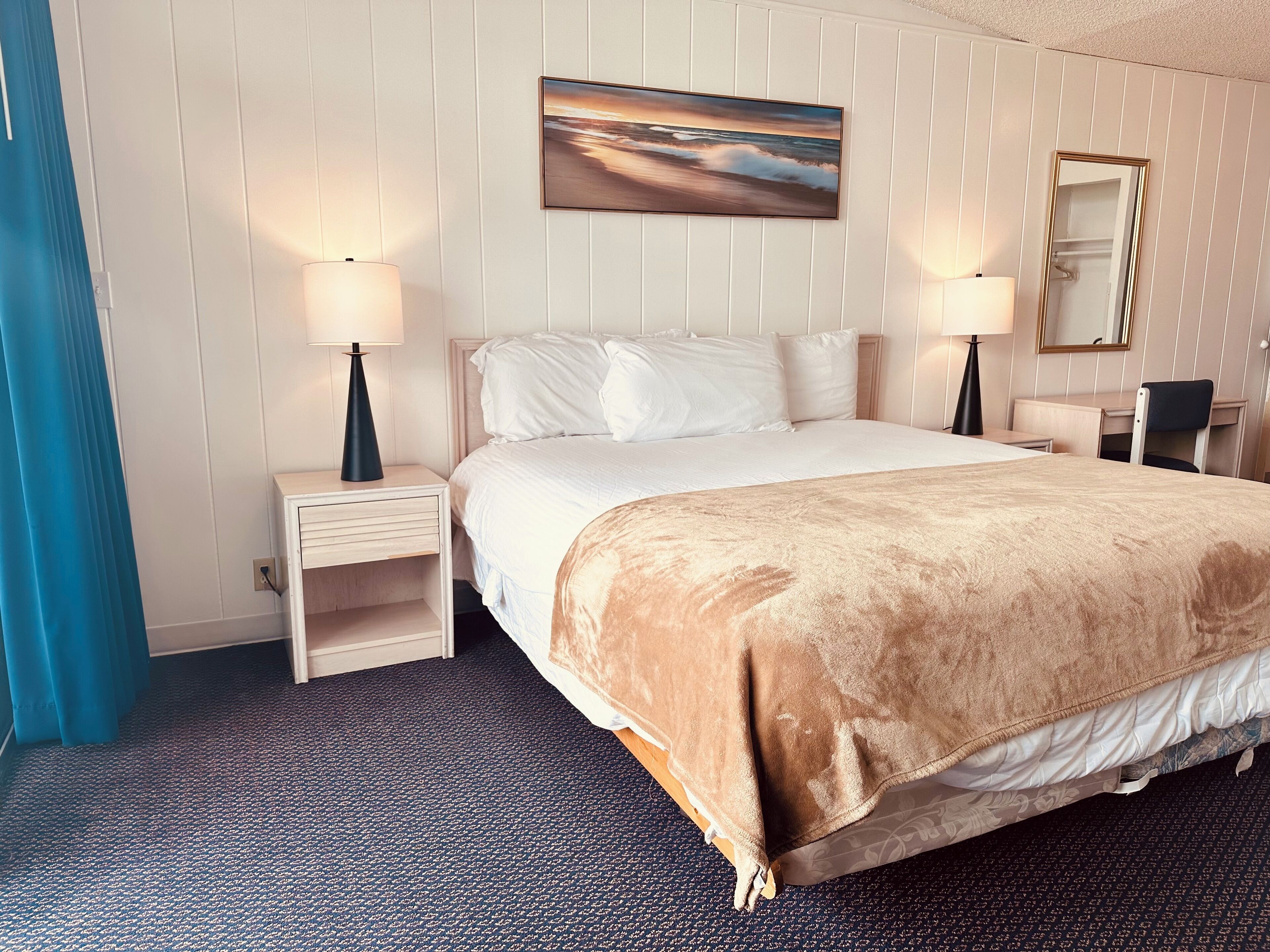Une chambre d’hôtel avec un grand lit, deux tables de chevet avec des lampes, un tableau au mur et un miroir au-dessus du lit.