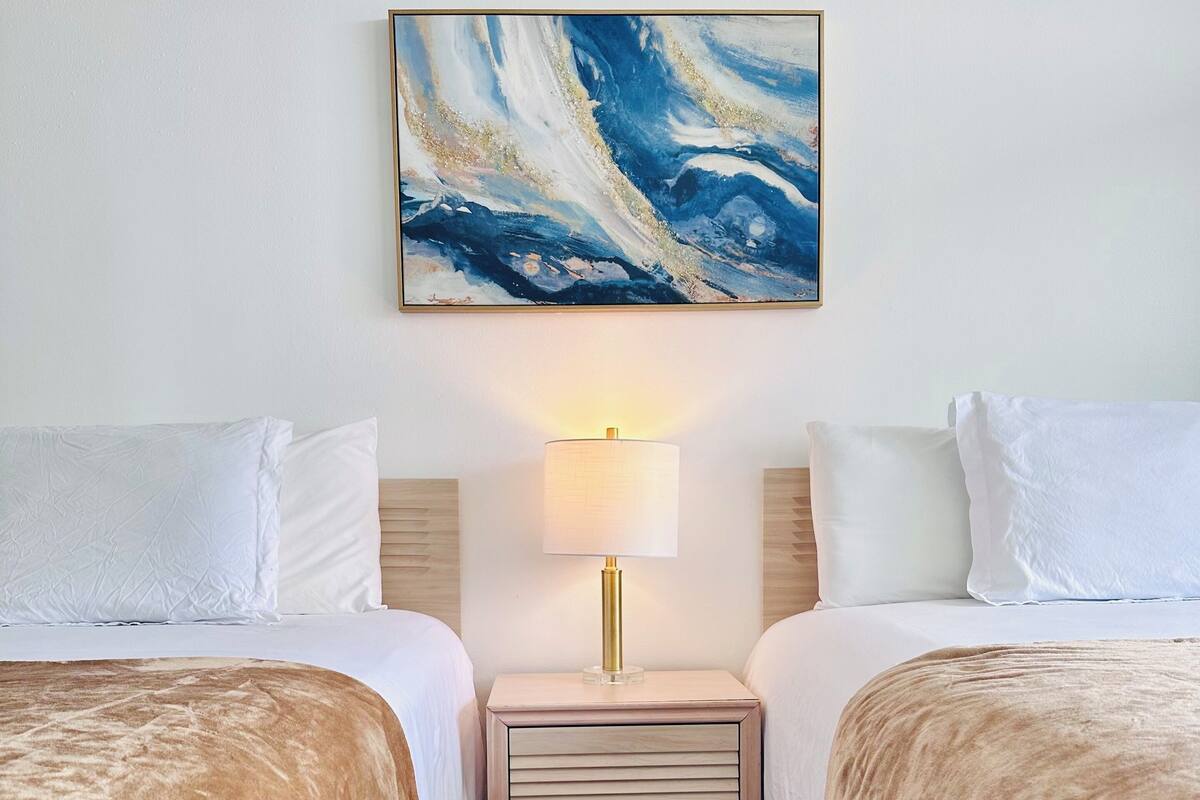 A hotel room with two beds, a nightstand with a lamp, and a painting on the wall.