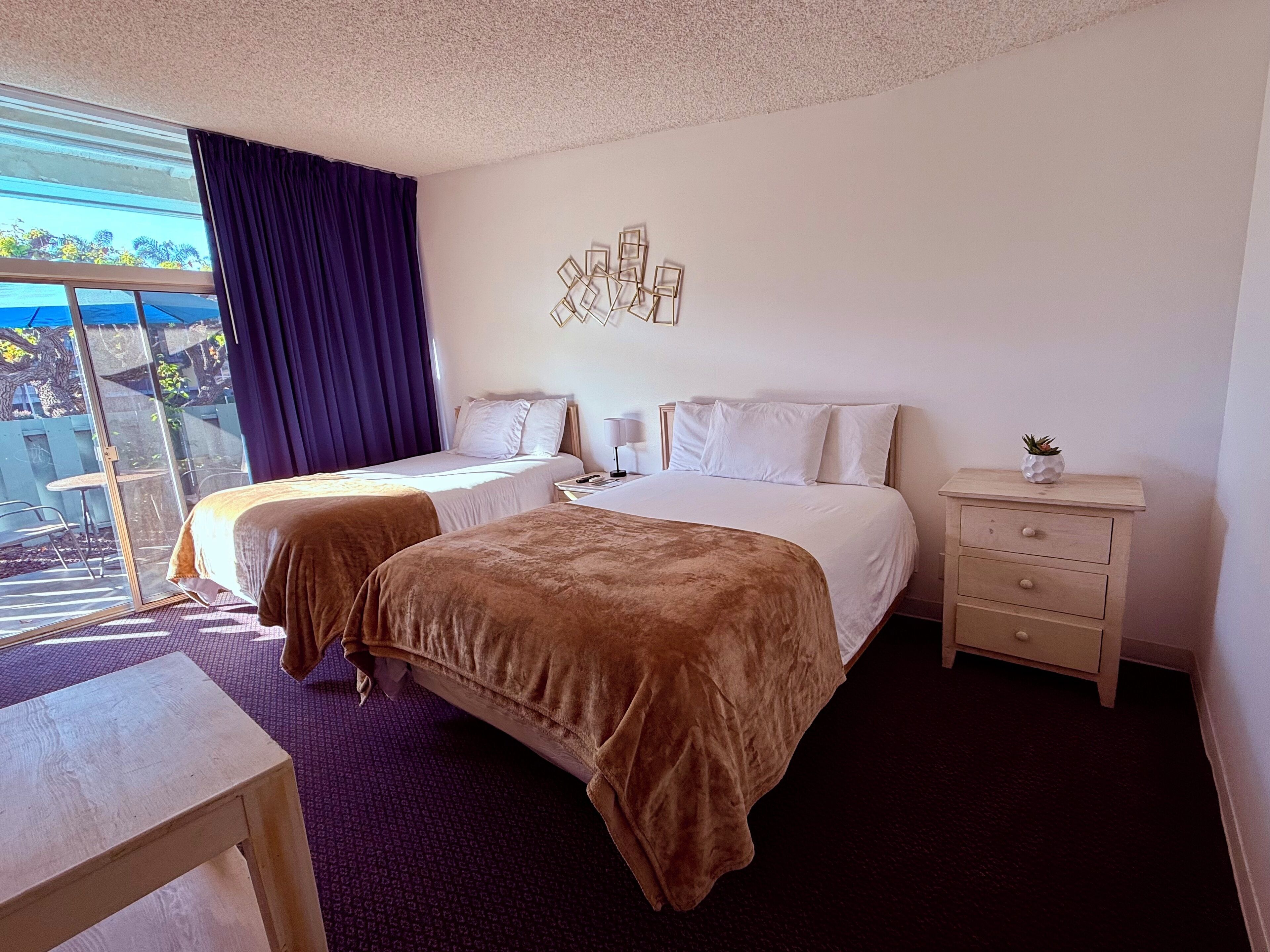 A hotel room with two beds, a desk, a nightstand, and a view of the outdoors.