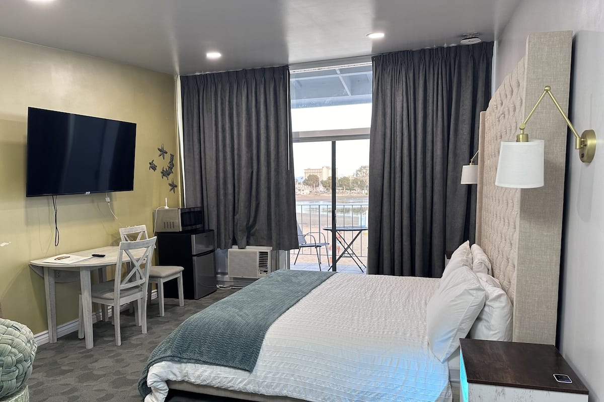 A hotel room with a bed, a desk, a TV, and a balcony with curtains.