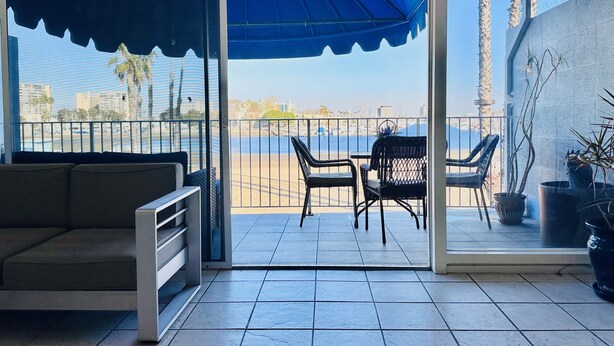 A balcony with a view of the beach, a sofa, and two chairs.
