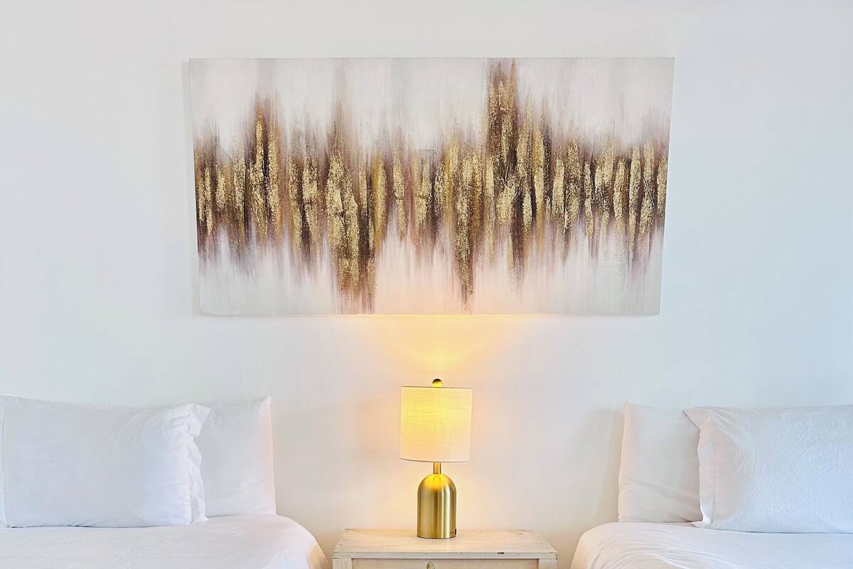 A hotel room with two beds, a nightstand with a lamp, a wooden floor, and a wall art piece.