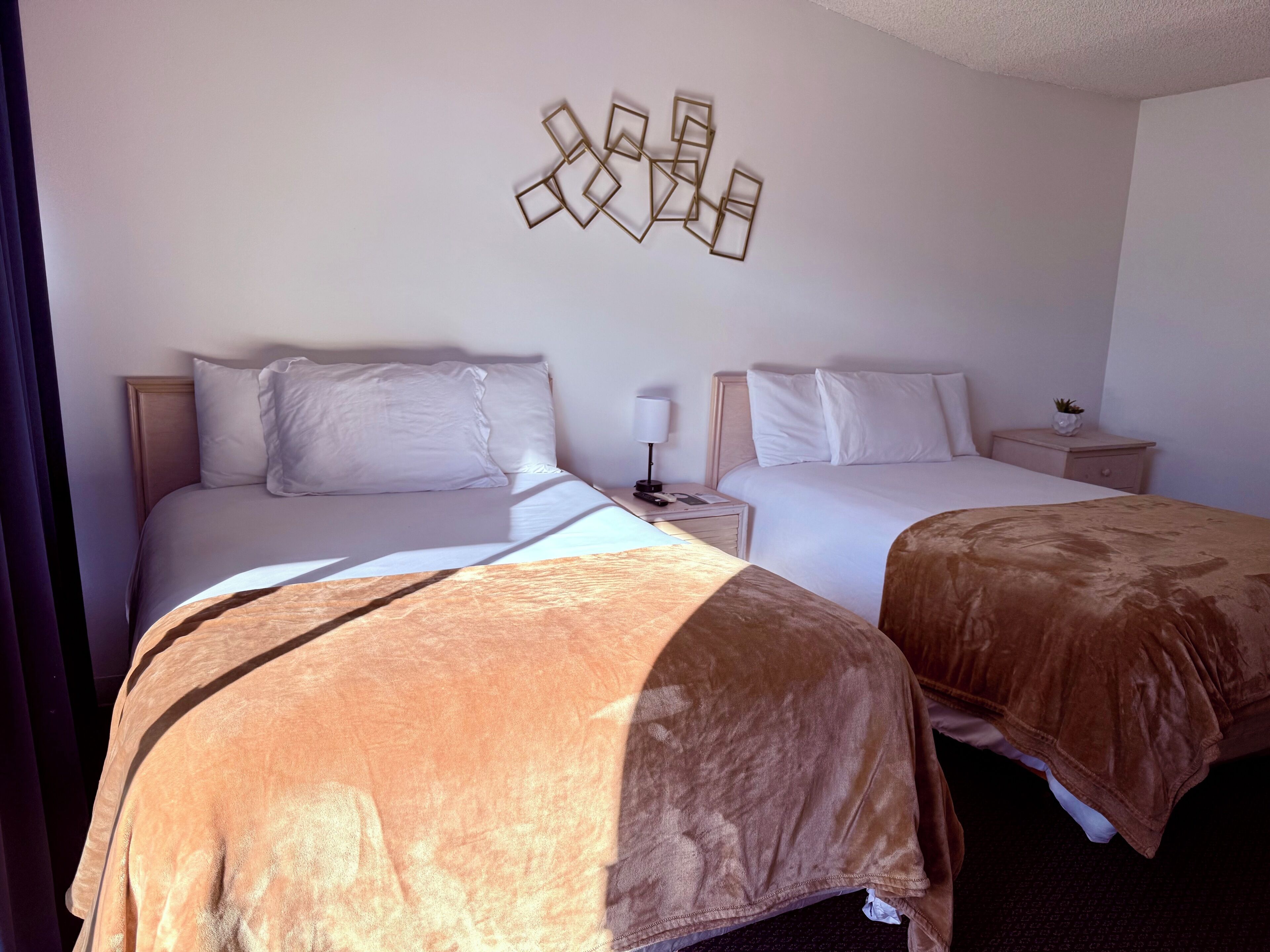 Une chambre d’hôtel avec deux lits, une table de chevet, une lampe et une œuvre d’art murale.