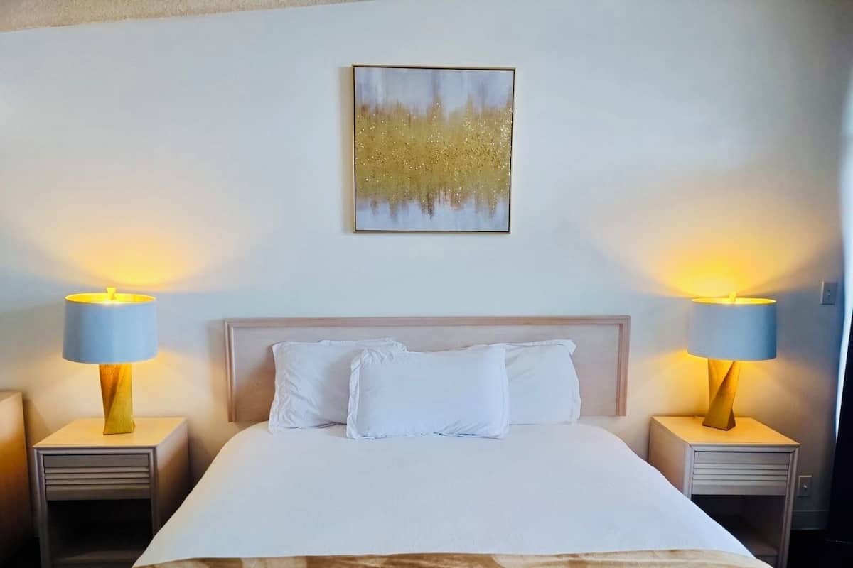 A hotel room with a large bed, two bedside tables with lamps, a headboard, and a wall-mounted artwork.