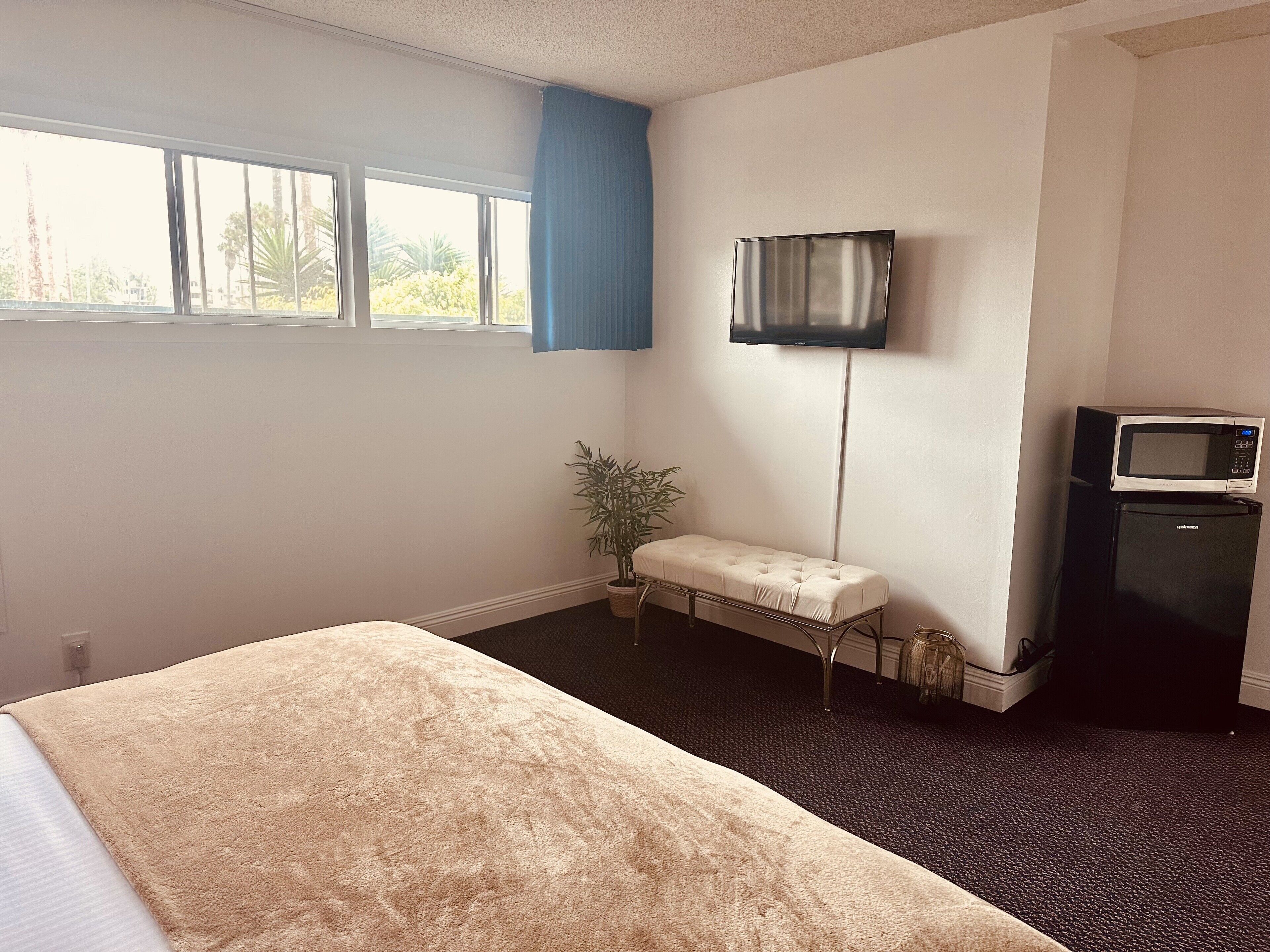 A hotel room with a bed, a small bench, a television, and a refrigerator.