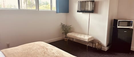 A hotel room with a bed, a small bench, a television, and a refrigerator.