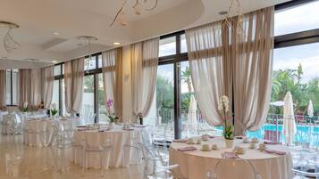 A spacious dining area with round tables, clear chairs, and large windows with curtains.