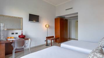 Quarto de hotel com cama, escrivaninha, cadeira, televisão e guarda-roupa.