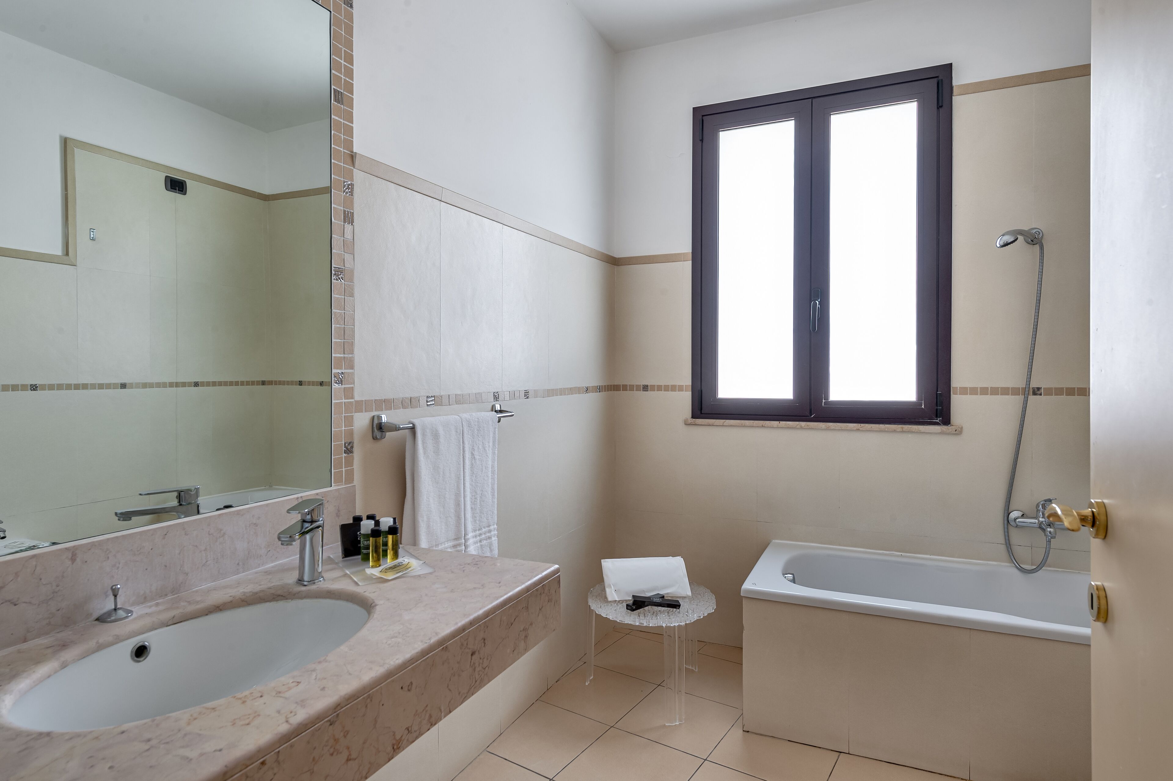 Un baño con bañera, lavamanos, una mesita y una ventana.