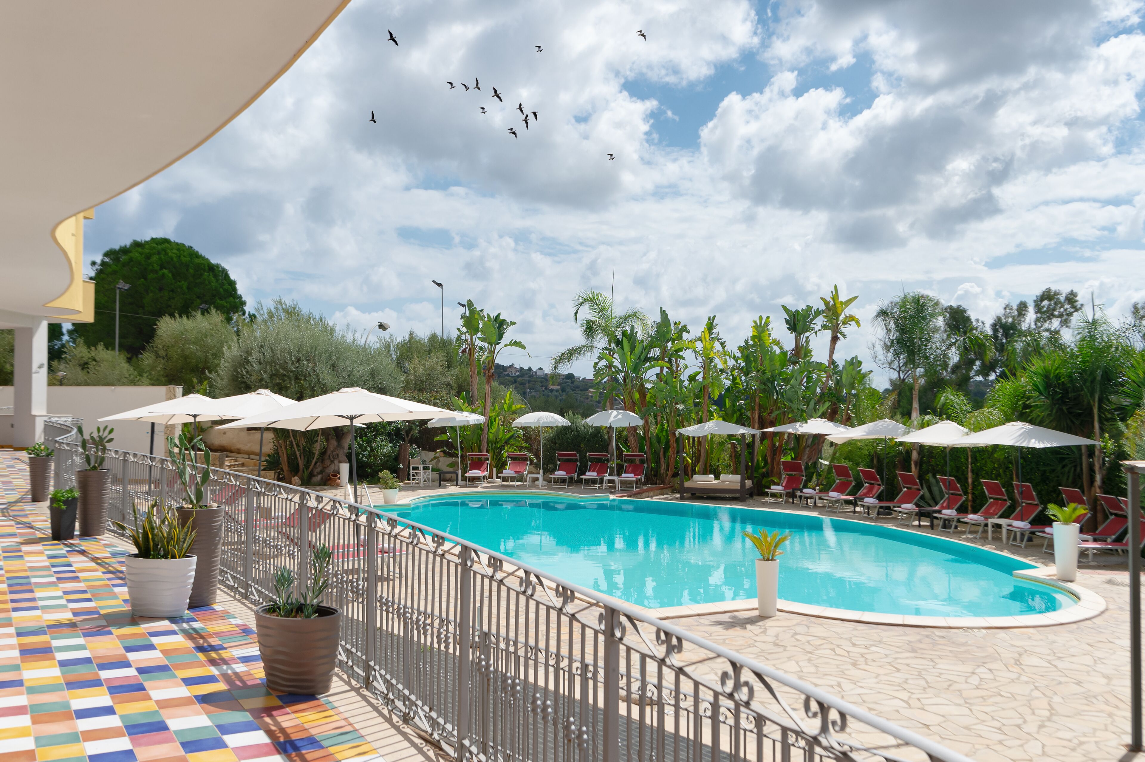 A swimming pool with lounge chairs and umbrellas, surrounded by potted plants and a tiled deck.