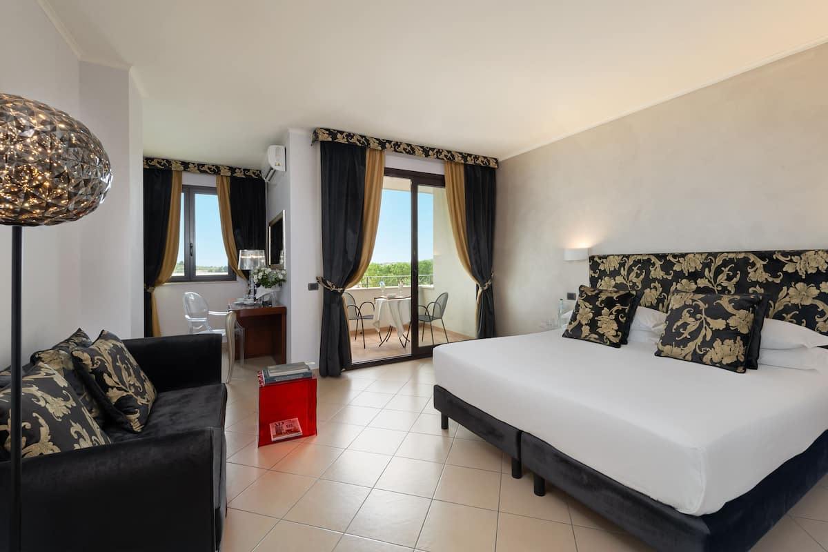 Une chambre d’hôtel avec un lit, un bureau, une chaise et un balcon avec des rideaux.