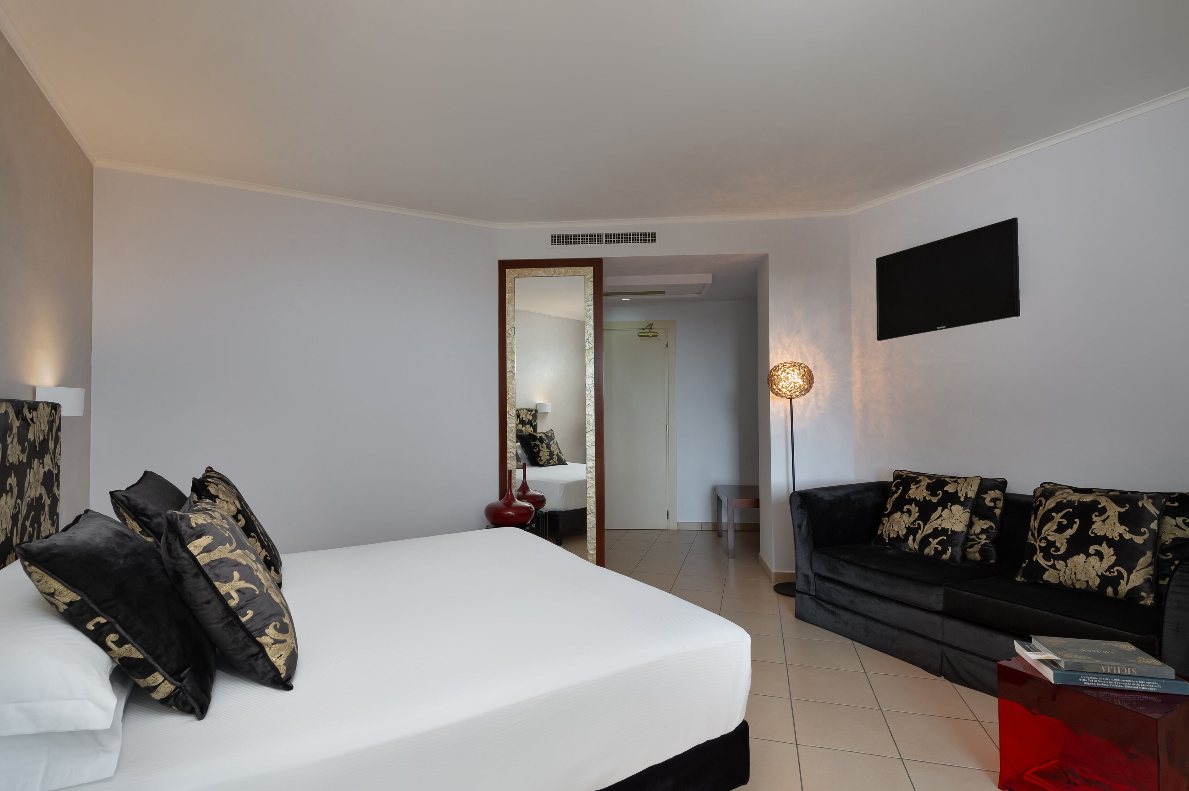 Una habitación de hotel moderna con una cama grande, un sofá negro, una mesita pequeña y un televisor montado en la pared.