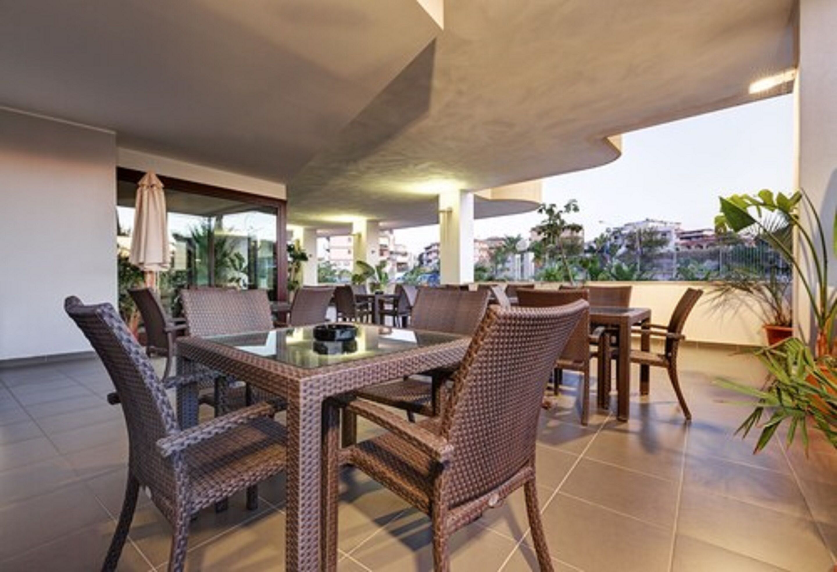 Une terrasse extérieure aménagée avec des meubles en osier, une table à plateau en verre et des plantes en pot.