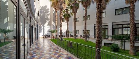 A corridor with a colorful tiled floor, palm trees, and a modern building with large windows.
