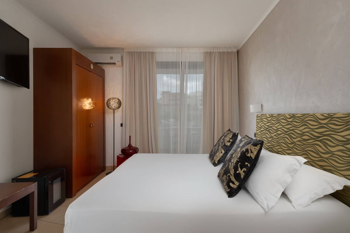 Une chambre d’hôtel avec un lit, un téléviseur fixé au mur, une armoire et une fenêtre avec des rideaux.