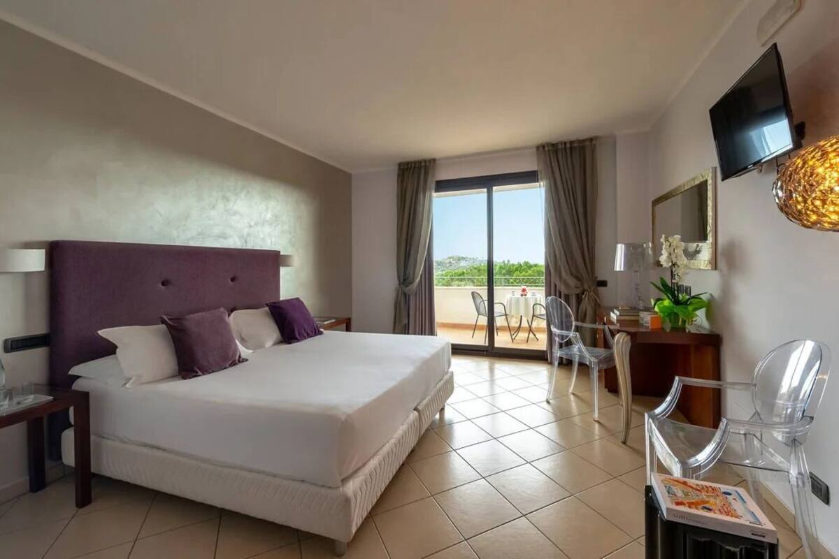 Une chambre d’hôtel avec un grand lit, un bureau avec une chaise, un téléviseur fixé au mur et un balcon avec vue.