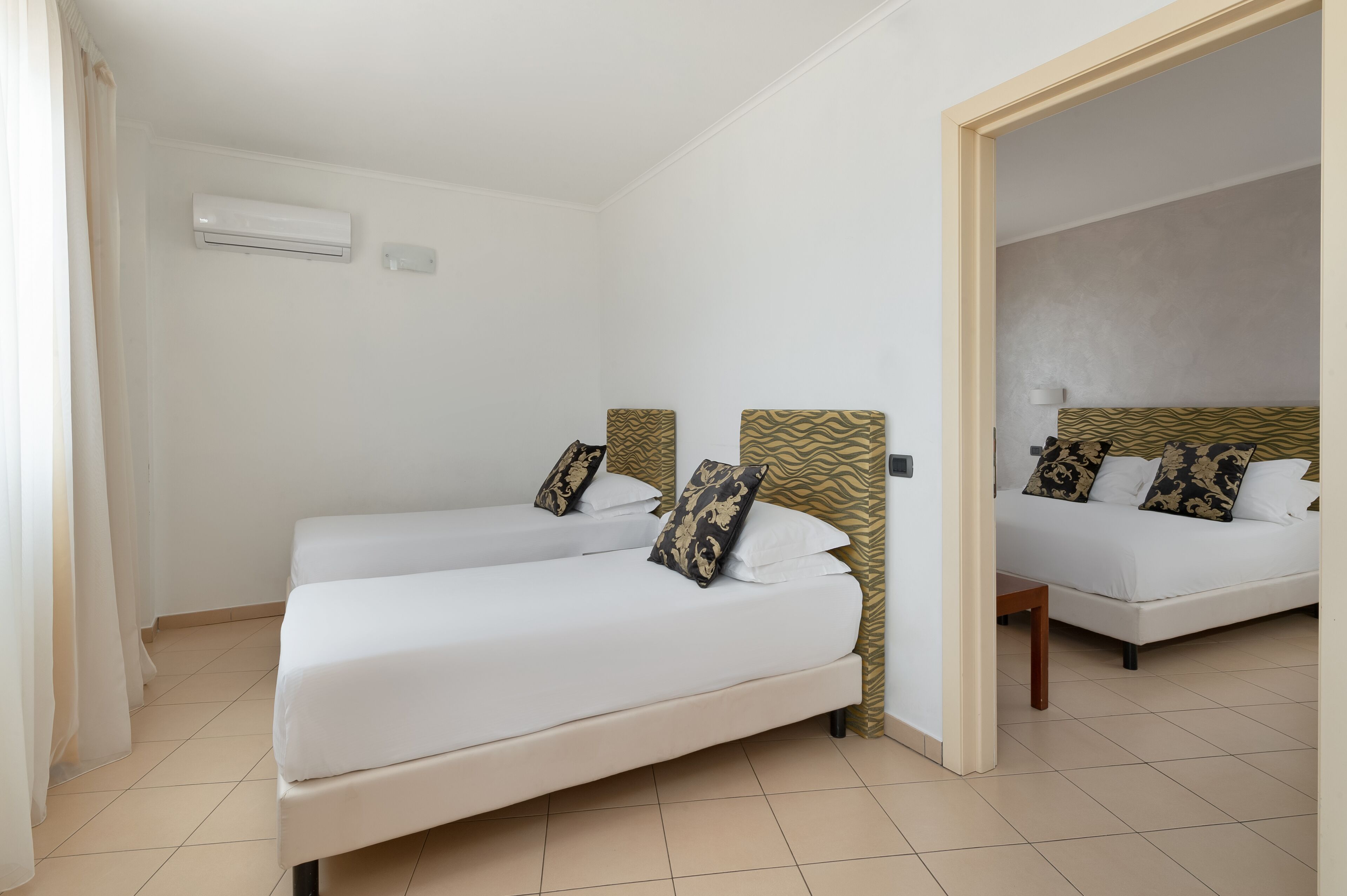 A hotel room with two single beds, a small table, and a mirror.