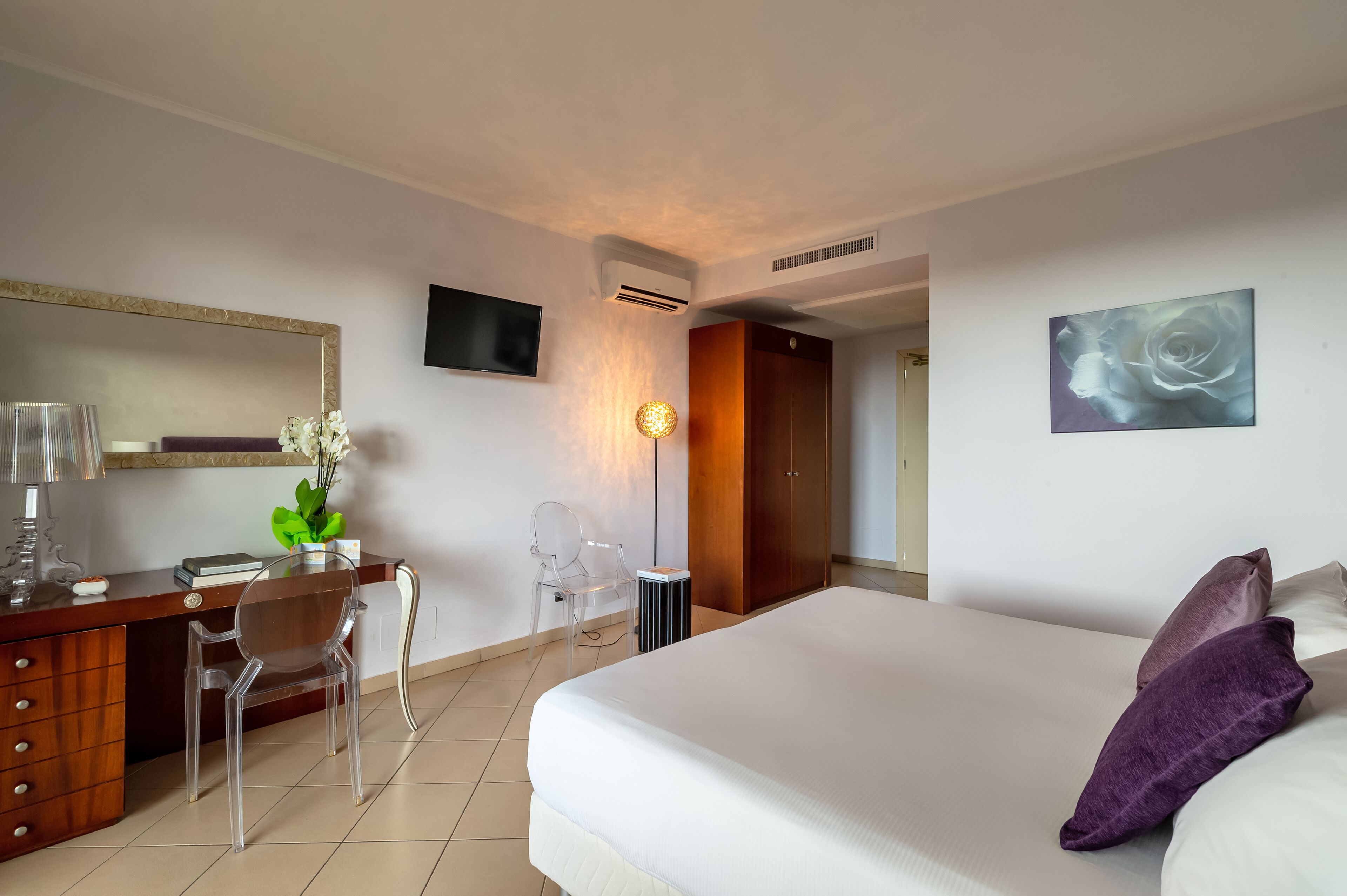 A hotel room with a bed, a desk with a chair, a TV, and a painting on the wall.