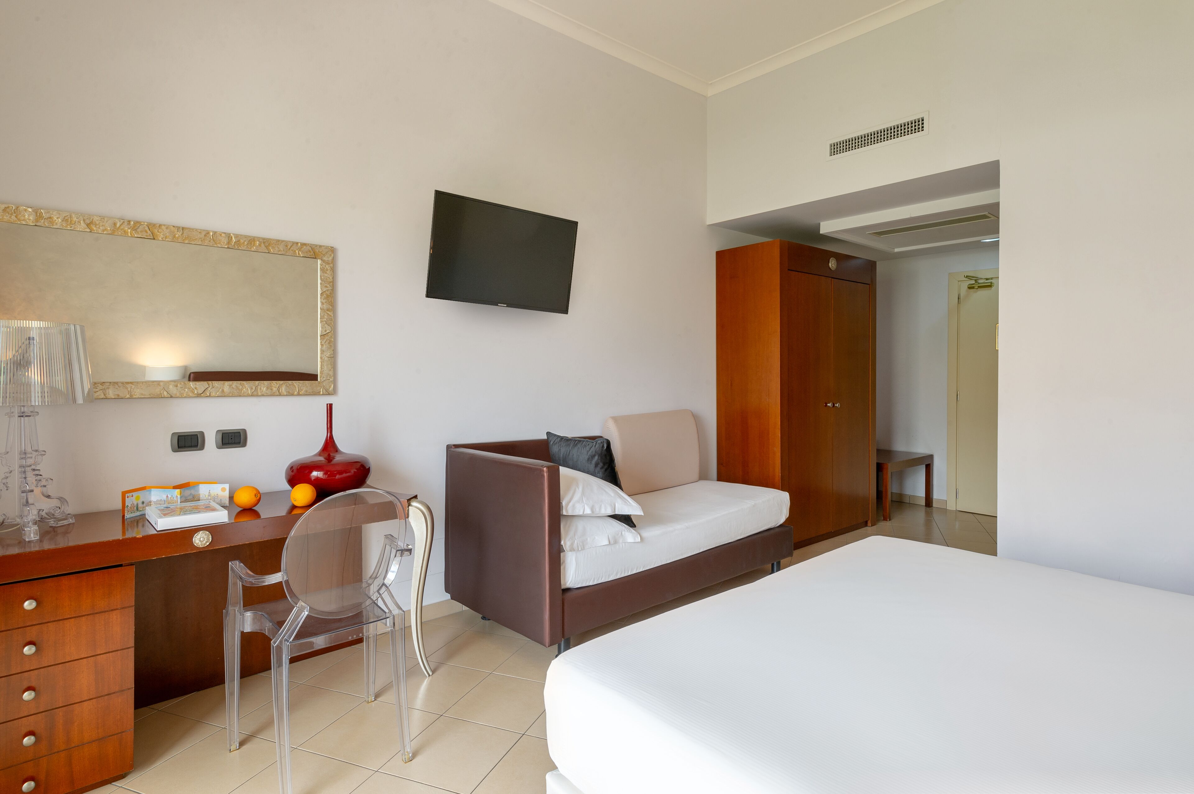 Une chambre d’hôtel moderne équipée d’un lit, d’un bureau avec une chaise, d’un téléviseur fixé au mur et d’une armoire.