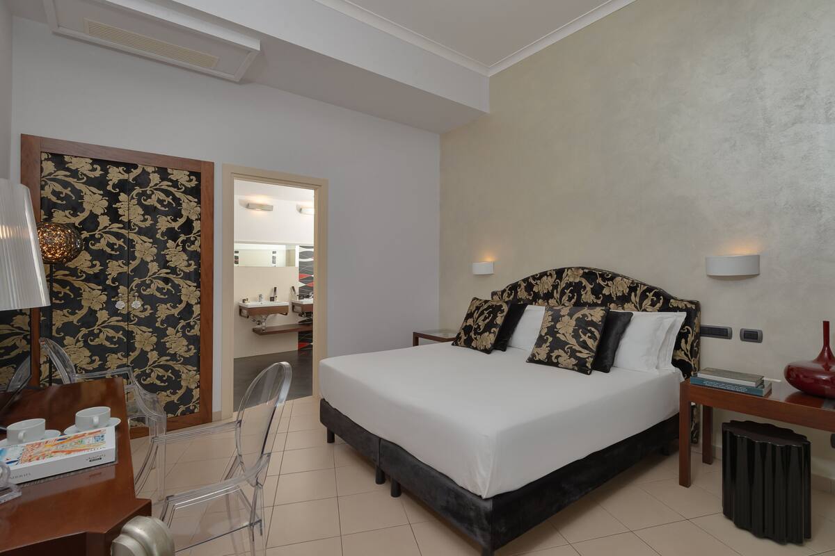 Une chambre d’hôtel comprenant un lit, une table de chevet, une lampe et un bureau avec une chaise.