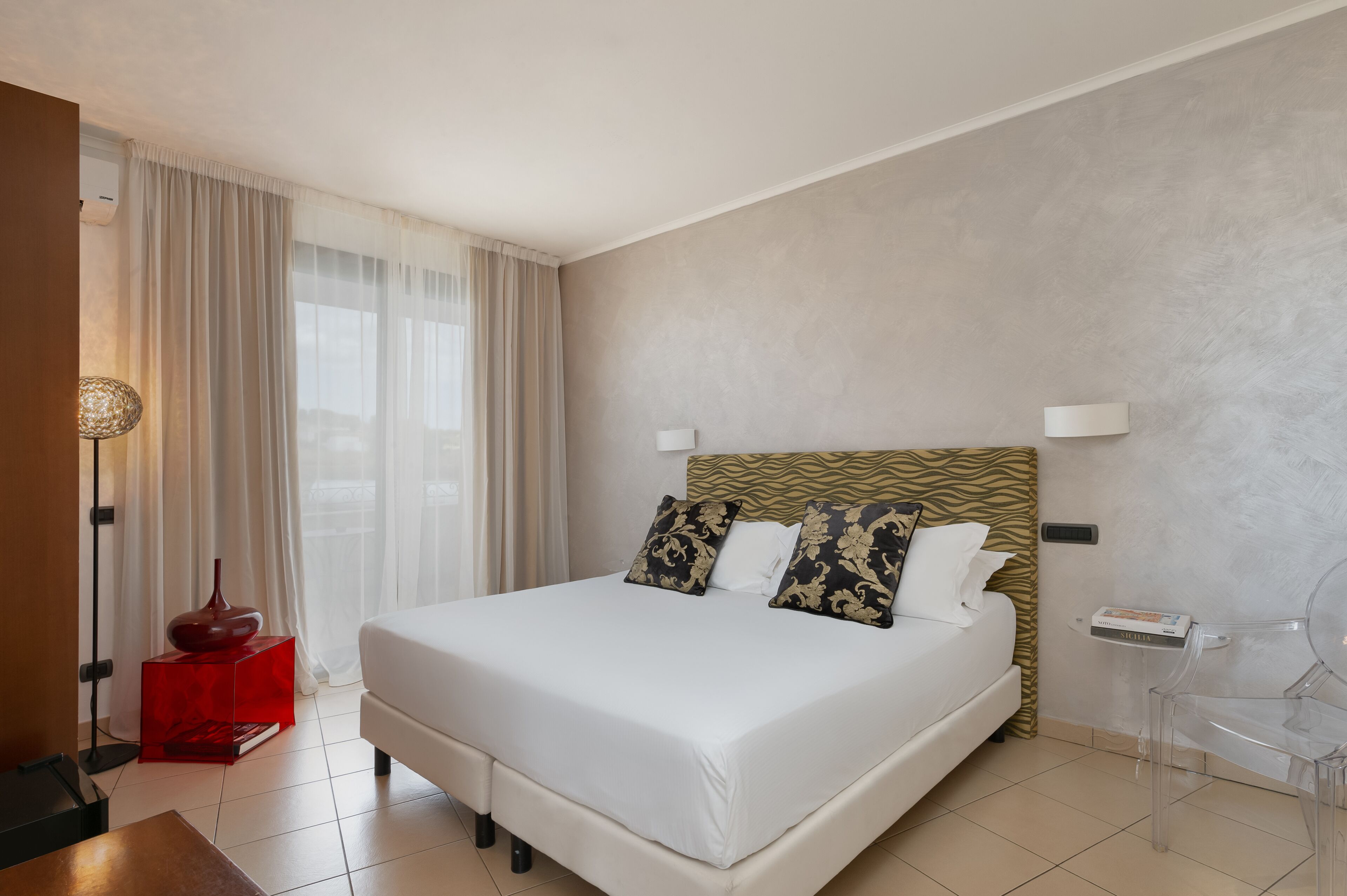 Una habitación de hotel moderna con una cama grande, un cabecero estampado con diseño de cebra y una mesita de noche roja.
