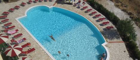 En swimmingpool med en stenbelagd poolkant, omgiven av solstolar och parasoller.