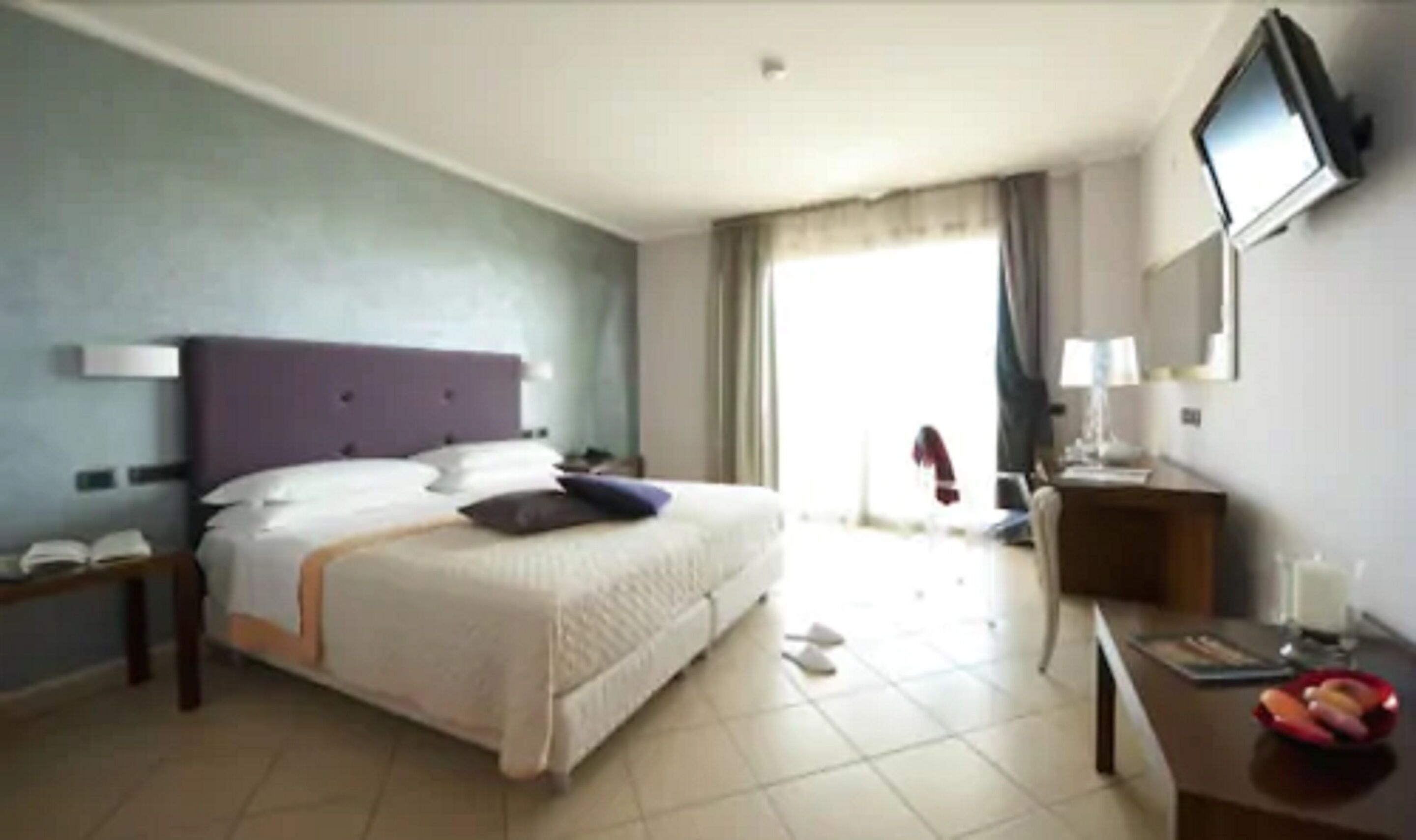 Une chambre d’hôtel avec un lit, un bureau, une télévision et une fenêtre avec des rideaux.