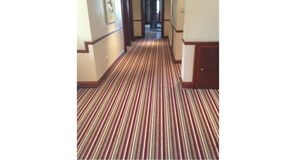 A hotel hallway with striped carpet, wooden doors, and framed artwork on the walls. - The Airman Hotel (Shefford)