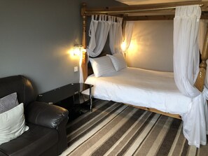 A single bed with a wooden frame and white bedding, a black leather sofa with cushions, and a striped carpet. - The Airman Hotel (Shefford)