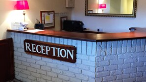 A reception desk with a sign labeled "RECEPTION," a mirror above it, and a lamp to the left. - The Airman Hotel (Shefford)