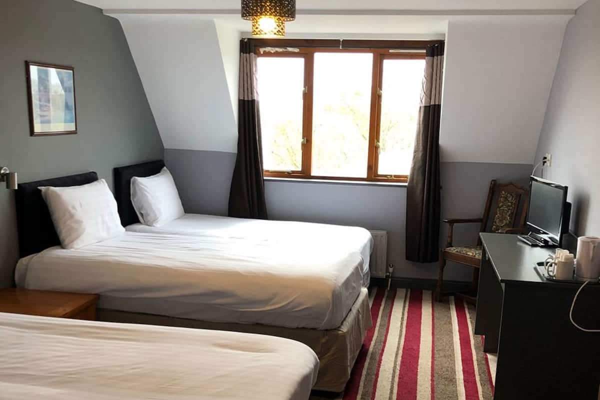 Ein Hotelzimmer mit zwei Betten, einem Schreibtisch mit Computer und einem Fenster mit Vorhängen.