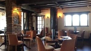 A restaurant with brick walls, wooden beams, and orange chairs. Tables are set for dining. - The Airman Hotel (Shefford)