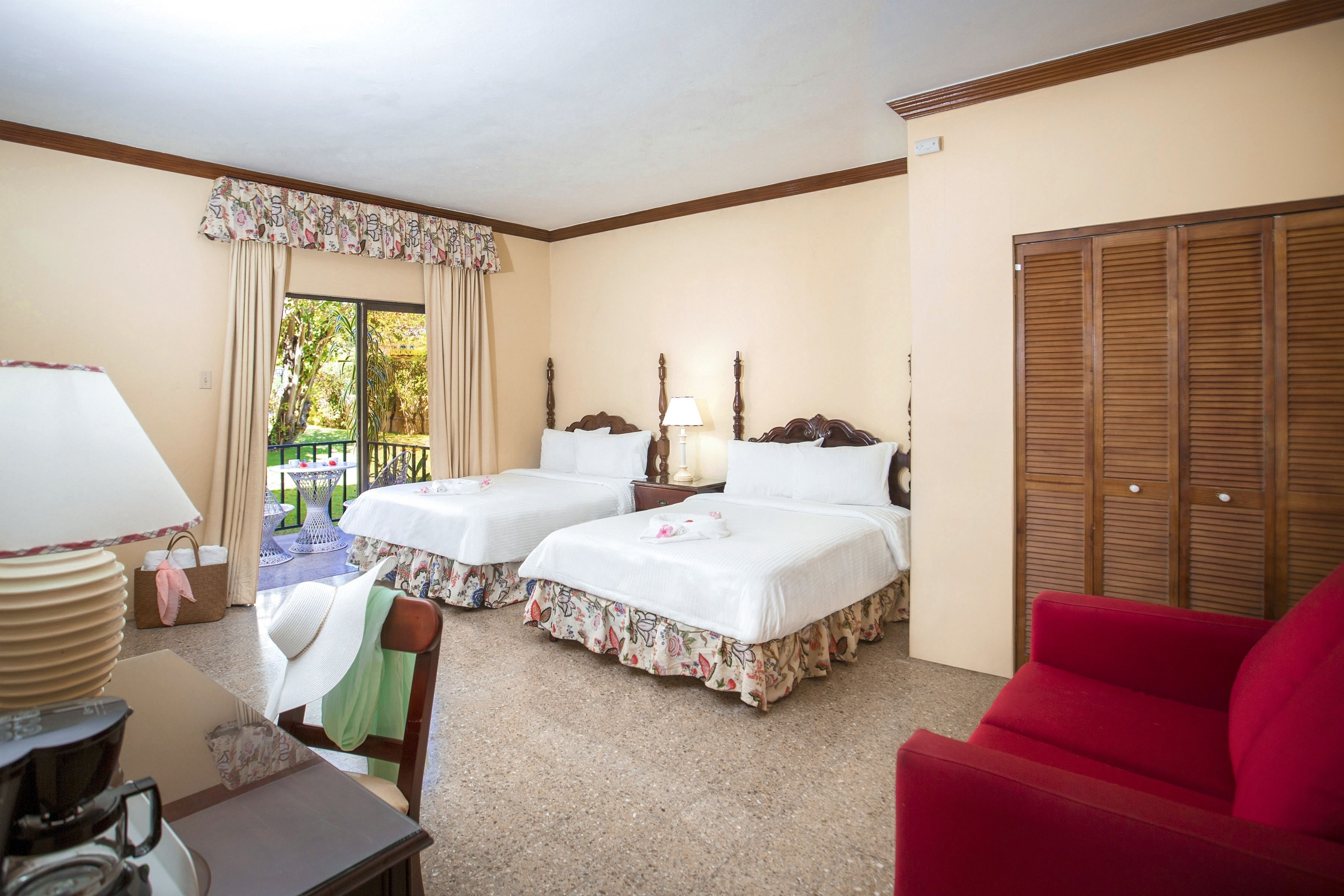 A hotel room with two beds, a red sofa, a table with a coffee maker, and a view of the outdoors.