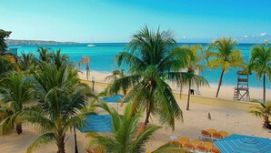 A beach with palm trees, a lifeguard tower, and lounge chairs under umbrellas. - Rooms on the Beach Negril (Negril)