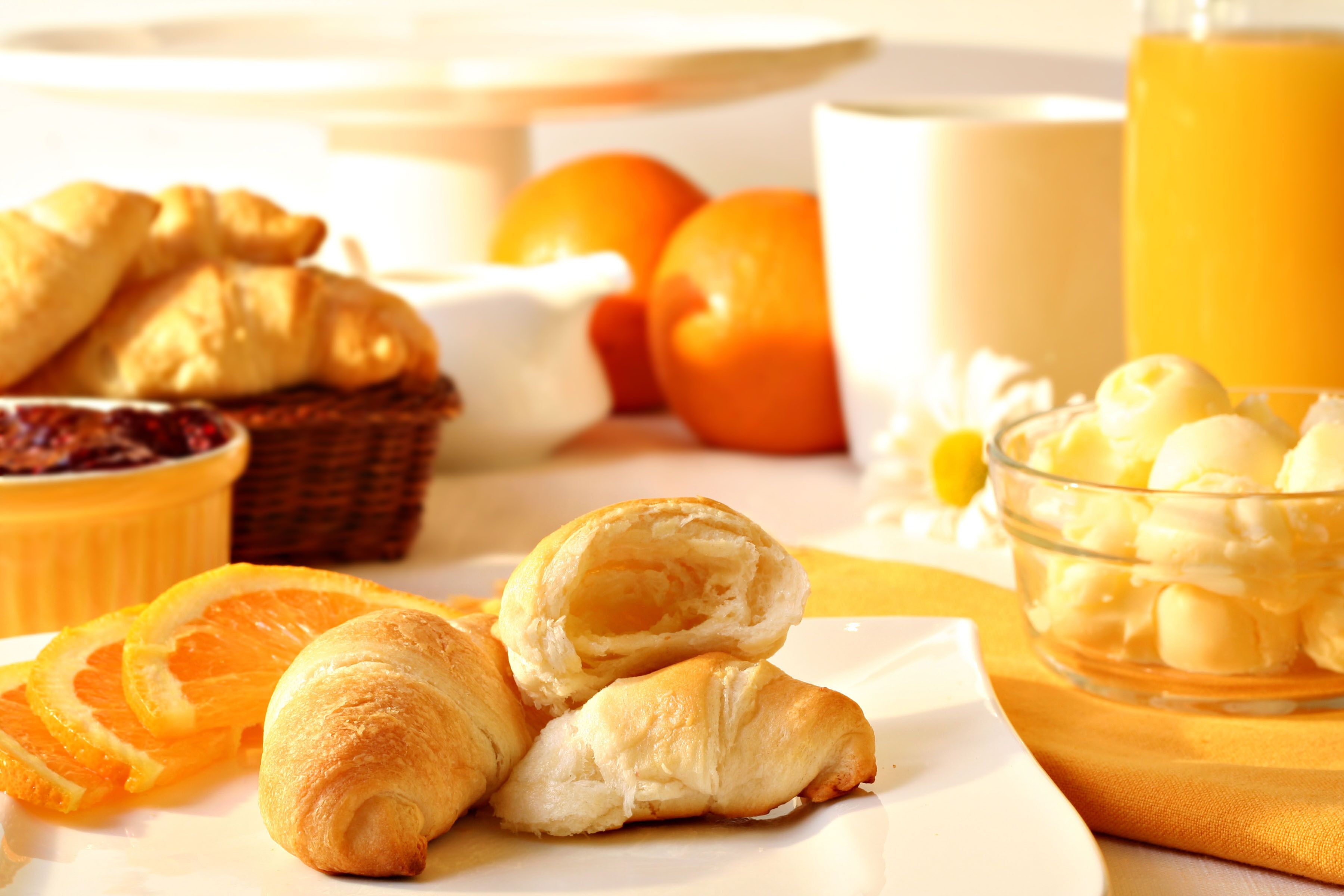 A breakfast setting with croissants, orange slices, a bowl of yogurt, and a glass of orange juice.