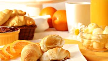 A breakfast setting with croissants, orange slices, a bowl of yogurt, and a glass of orange juice.