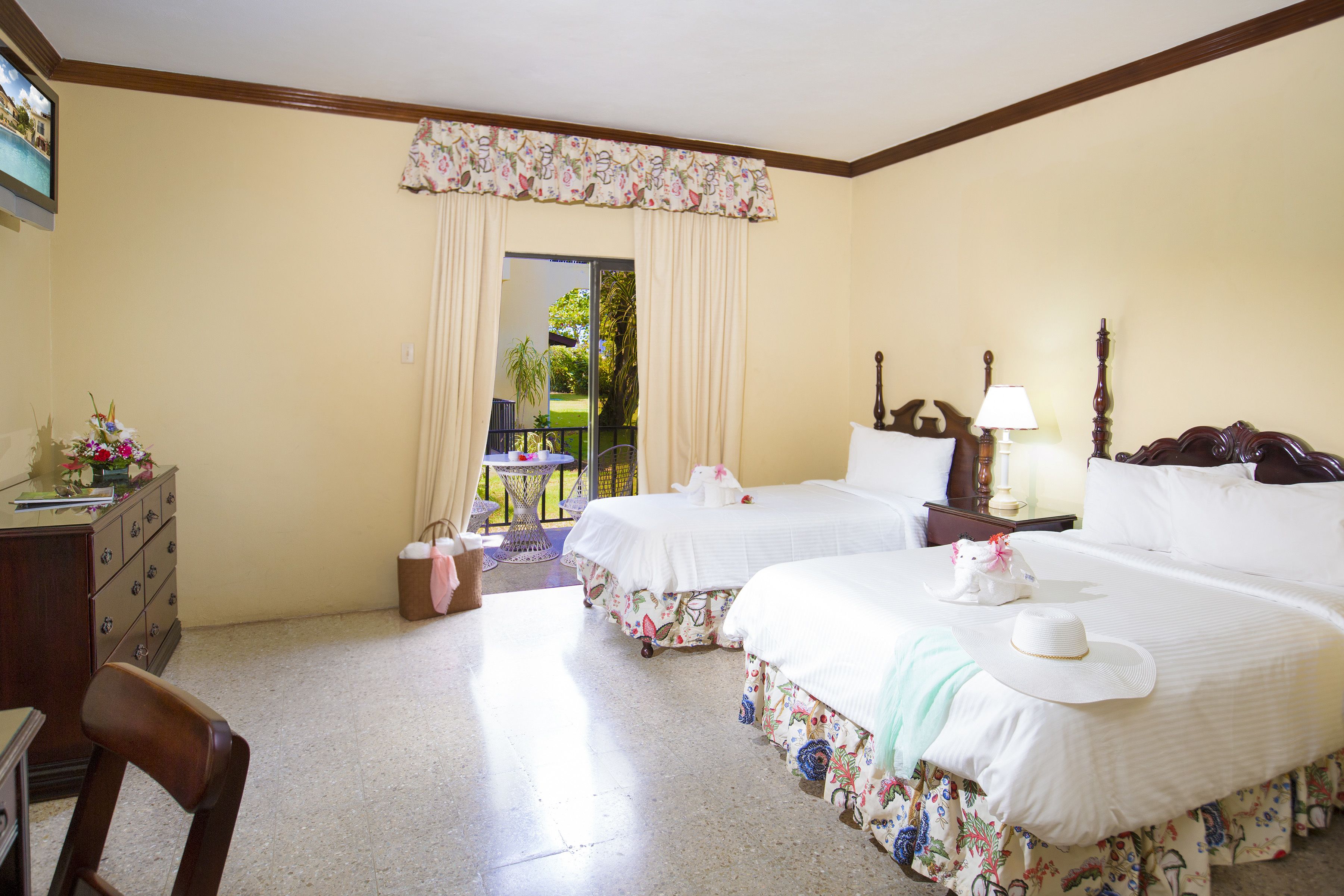 A hotel room with two beds, a desk, a chair, a small table, and a view of the outdoors.