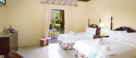 A hotel room with two beds, a desk, a chair, a small table, and a view of the outdoors.