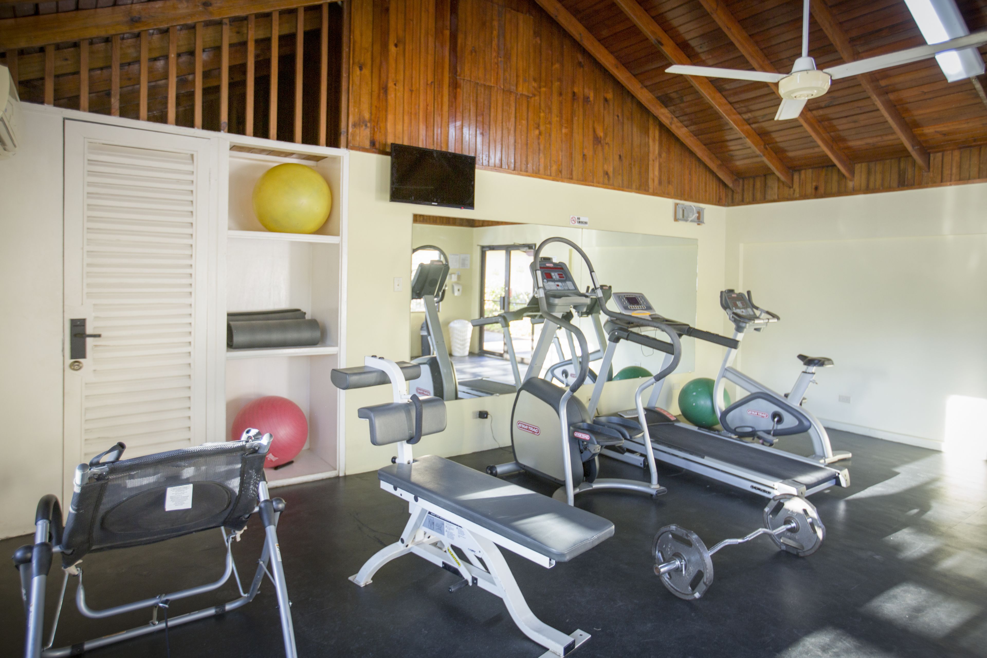 Une salle de sport équipée de tapis de course, de ballons d’exercice et d’un banc.