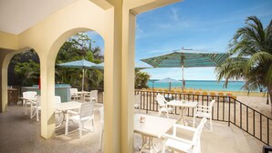 An outdoor patio with white tables and chairs, a pool, and a view of the beach. - Rooms on the Beach Negril (Negril)